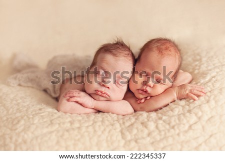 Newborn twins sleeping on the beige blanket together
