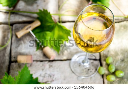 Glass of white wine on top of the background of stone, corkscrew and cork, vine leaves and grapes.