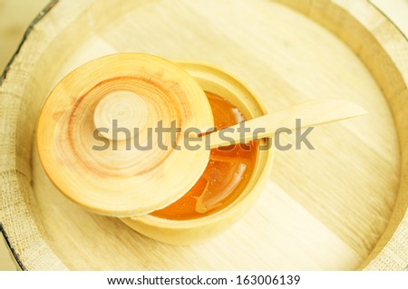 Honey in a wooden bowl with a wooden spoon and lid. Background wooden barrel