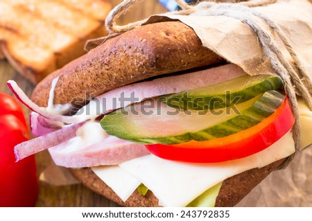 Sandwich with ham, cheese, lettuce and pickles in fast food packaging