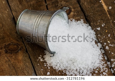 Salt spill out of the bucket tin on a wooden board. Rustic style