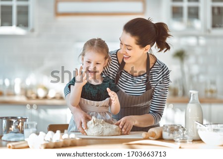 Happy loving family are preparing bakery together. Mother and child daughter girl are cooking cookies and having fun in the kitchen. Homemade food and little helper.                                  