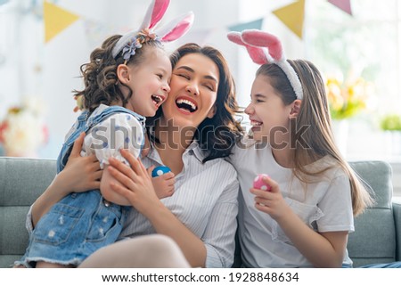Happy holiday! Mother and her daughters with painting eggs. Family celebrating Easter. Cute little children girls are wearing bunny ears. 