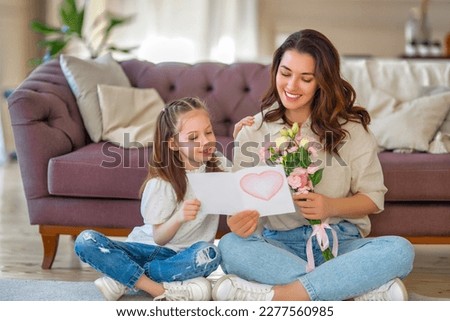 Similar – Image, Stock Photo Child daughter congratulates mother and gives present card, gift and bouquet of flowers at home. Mom and girl smiling and hugging on couch. Happy mothers day celebration