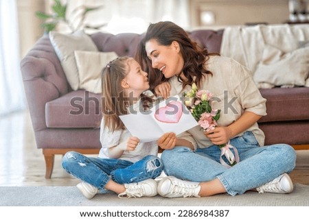 Similar – Image, Stock Photo Child daughter congratulates mother and gives present card, gift and bouquet of flowers at home. Mom and girl smiling and hugging on couch. Happy mothers day celebration