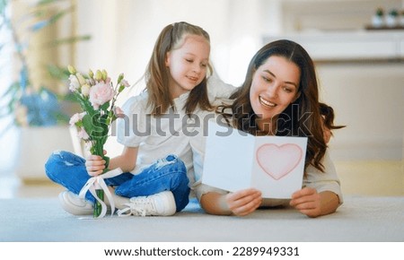 Similar – Image, Stock Photo Child daughter congratulates mother and gives present card, gift and bouquet of flowers at home. Mom and girl smiling and hugging on couch. Happy mothers day celebration