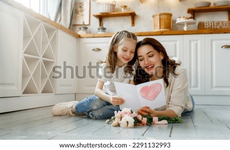 Similar – Image, Stock Photo Child daughter congratulates mother and gives present card, gift and bouquet of flowers at home. Mom and girl smiling and hugging on couch. Happy mothers day celebration