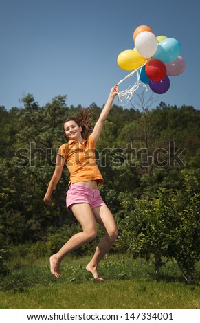 Beautiful and athletic Girl jumping with balloons on a green meadow