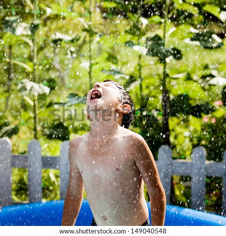 Happy little boy pours water from a hose
