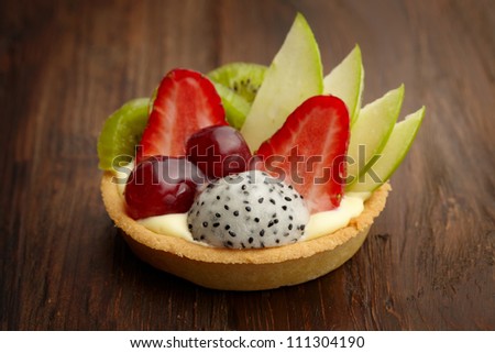 mixed fruit tart ; strawberry, grape, kiwi, apple and dragon fruit ; on wooden background under studio light