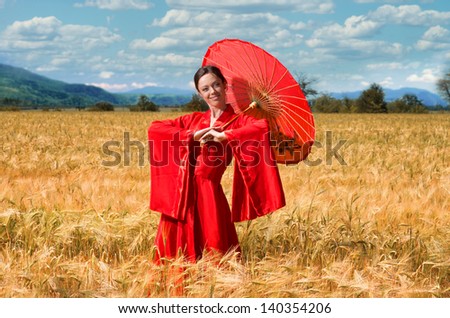 Woman in red clothes with chinese umbrella posing in the wheat field