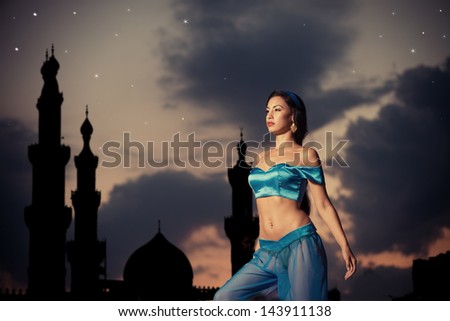 Arabian nights. Beautiful girl in belly dance costume with a silhouette of eastern palace in the starry sky