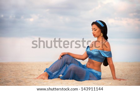 Beautiful brunette girl in belly dance costume sitting on the sand at sunset