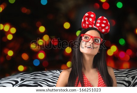 Portrait of a funny girl with a big hair bow and glasses looking up with colorful lights on dark background