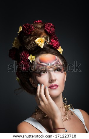 Portrait of a woman in art make-up and hair style with flowers looking up, dark background