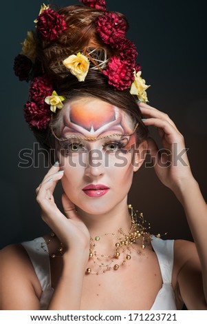 Portrait of a woman in art make-up and hair style with flowers looking at camera, dark background