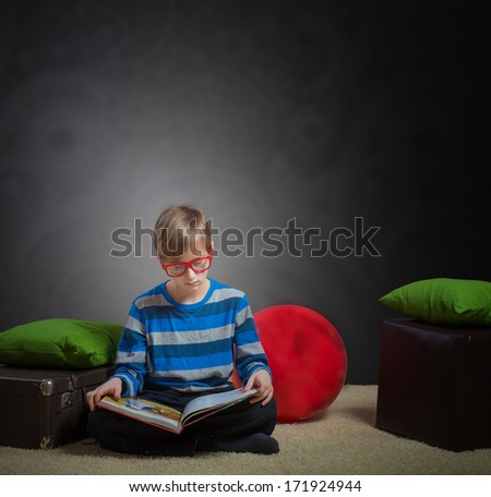 Serious preteen boy sitting on the floor and reading a book, dark background