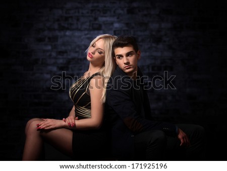 Handsome young couple sitting back to back in the darkness