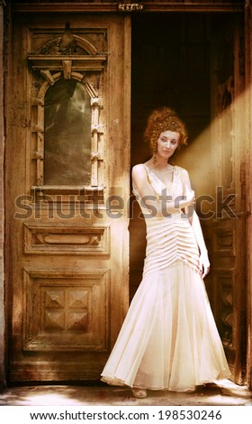 Portrait of young pretty girl in long dress standing in front of the old door