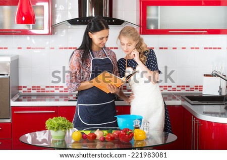 Two women in the kitchen cook using cookbook