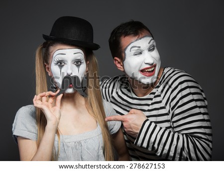 Female mime with paper mustaches, male mime laughing at her