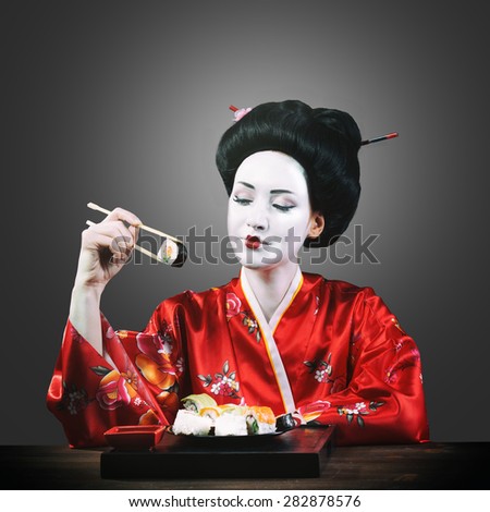 Woman in geisha makeup eating sushi, gray background