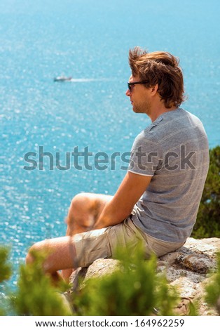 Young Man relaxing Outdoor on rocky cliff sitting and looking on Sea Summer time Traveling Lifestyle