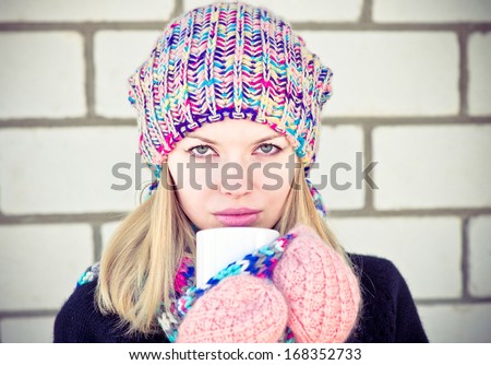 Winter Woman with coffee cup wearing knitted sweater, hat and scarf with mittens Lifestyle concept trendy colors white brick wall on background