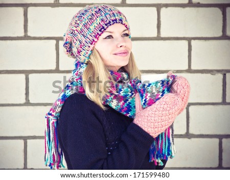 Young Woman happy smiling Face with coffee cup Winter time wearing knitted sweater, hat and scarf with mittens Lifestyle concept with white brick wall on background
