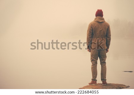 Young Man standing alone outdoor with foggy scandinavian nature on background Travel Lifestyle and melancholy emotions concept film effects colors