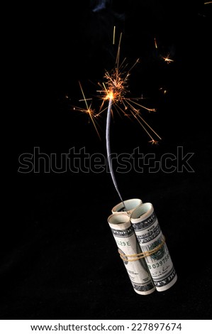 A roll of cash made into a dynamite stick has a lighted fuse throwing smoke and sparks before it explodes.