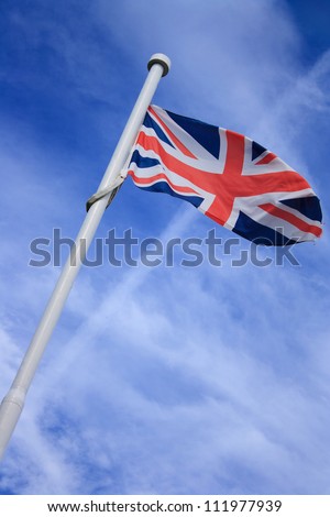 union jack flag on a flagpole waving in the wind, with blue sky and fluffy clouds in the  background