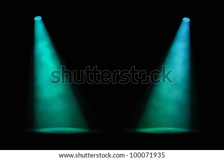 Two blue-green spotlights shining at a slight angle from either side of an empty stage with a foggy atmosphere and dark background