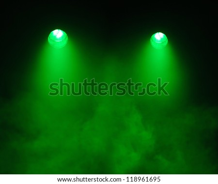 Two broad beamed green spotlights shining straight down through a very smoky atmosphere in darkness with the electrical elements visible in the lights