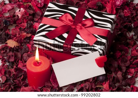 red gift box with paper label and candle on rose petals