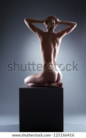 Nude young woman sitting on cube in studio