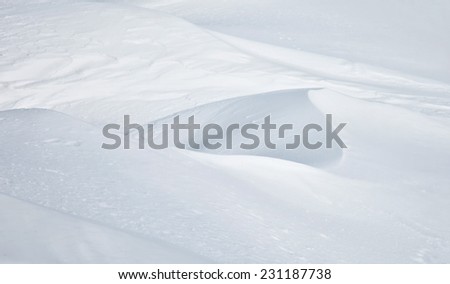Abstract detail of drifting snow catching late afternoon light showing blurry gentle ridges with soft highlights and shadow.