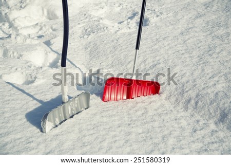 Two, red and silver color, snow shovels for snow removal in deep fresh snow.