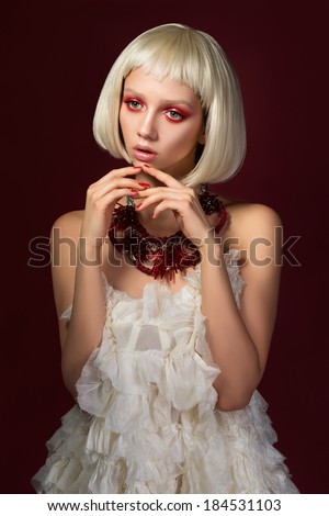 Young innocent woman in red necklace and white dress over red background