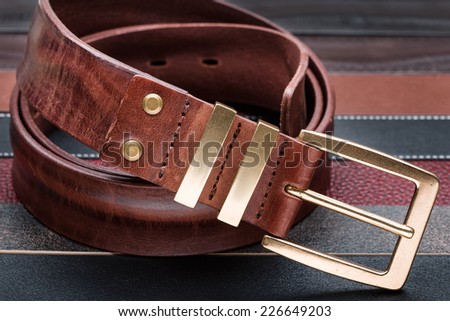 Brown men leather belt with golden buckle over leather strips background