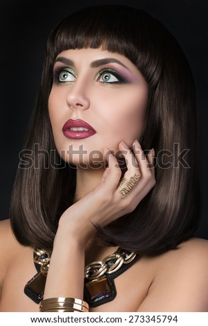 Portrait of beautiful tanned brunette woman touching her face and wearing golden bijouterie