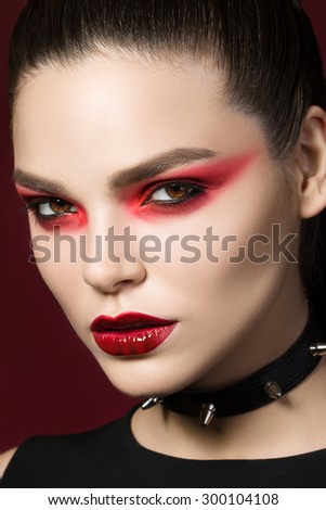 Young beautiful gothic woman with white skin and red lips with bloody drops wearing black collar with spikes. Red smokey eyes. Halloween make-up.