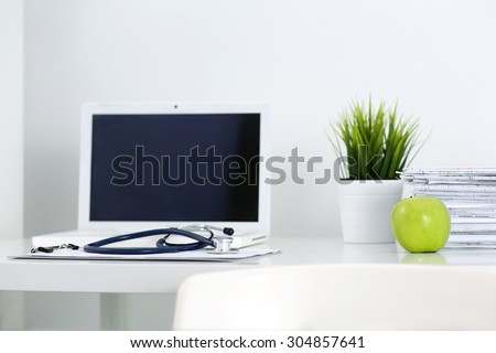 Medicine doctor\'s working table. Laptop, papers, green apple and stethoscope lying on table at physician\'s office. Healthcare and medical concept