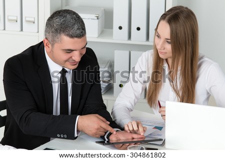 Young beautiful business woman consulting with her male colleague showing something on tablet PC. Partners discussing documents and ideas