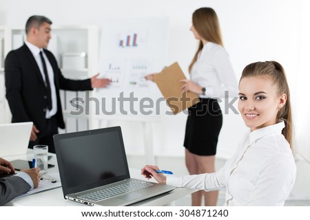 Business people meeting in office to discuss project. Young pretty female office worker looking at camera with her colleagues acting on background. Business meeting and teamwork concept