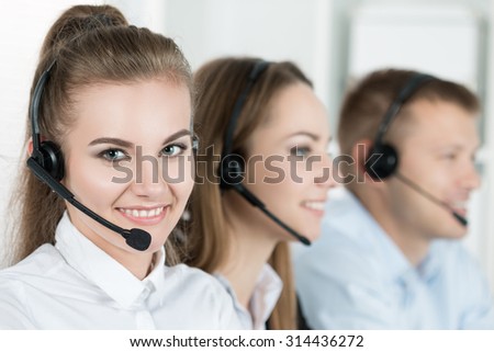 Portrait of call center worker accompanied by her team. Smiling customer support operator at work. Help and support concept