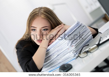 Tired business woman laying on heap of papers at her working place. Overwork, working overtime and stress at work concept.