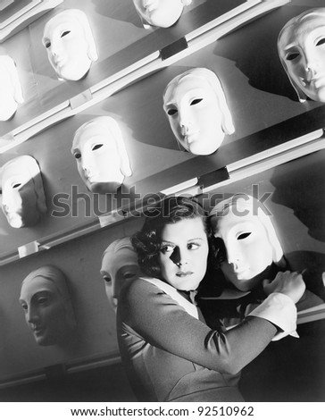 Woman looking frightened holding onto one mask on the wall of masks