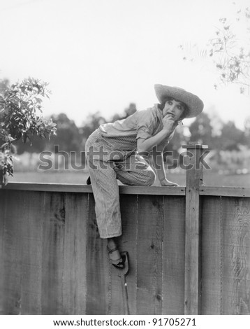 Young woman trying to get over a wooden fence with a fruit in her hands