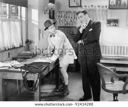 Two men standing in an office, one ironing his pants